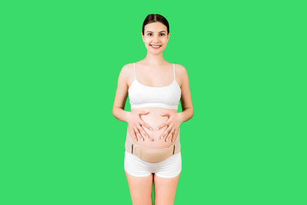 Yeşil arka planda fotokopi çekilen sırt ağrısını azaltmak için iç çamaşırı giymiş hamile bir kadının portresi. Ortopedik abdominal destek kemeri kavramı. - Fotoğraf, Görsel