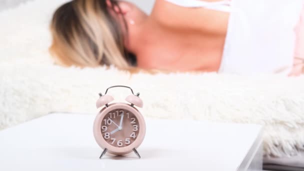 寝室のテーブルの上の目覚まし時計。女性の背景で寝て、選択的な焦点。新しい一日を始めるというコンセプト. - 映像、動画