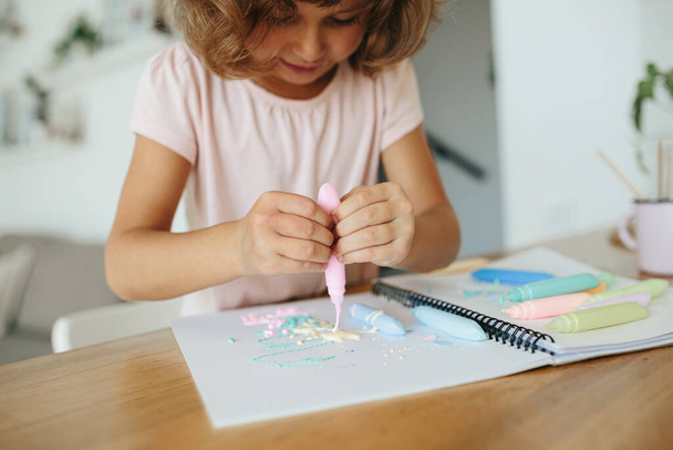 Little girl, preschooler, child painting at the table in a white living room at home close up on paint in tubes selective focus. Home schooling concept - Photo, Image