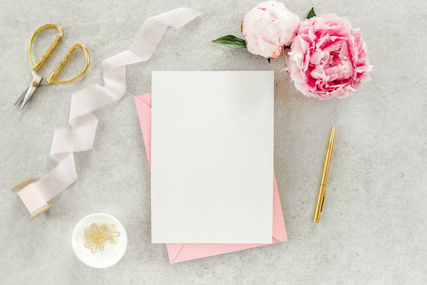 Mockup invitation, blank paper greeting card, pink envelope and peonies on gray stone table. Flower background. Flat lay, top view. - Foto, Imagem