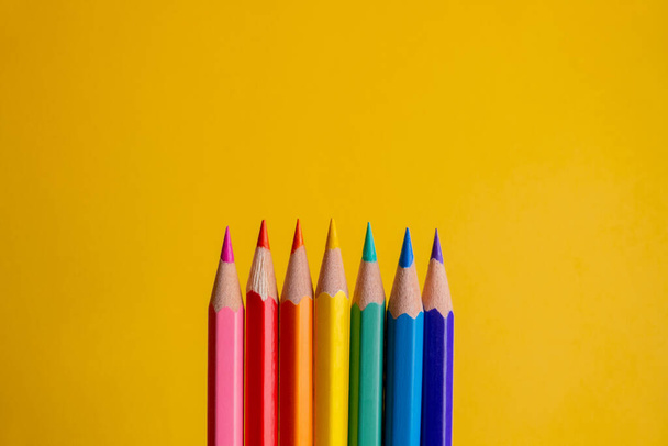 hét színes ceruza a középső sorban sorrendben és gradiens színben, olyan színekkel, mint a rózsaszín, kék, zöld, piros, narancs és sárga, jó tippekkel és sárga homályos háttérrel, lgbt-szerű színekkel - Fotó, kép
