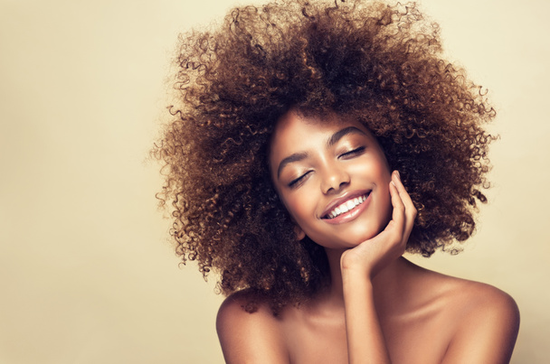 Ομορφιά πορτρέτο της αφρικανικής Αμερικής γυναίκα με καθαρό υγιές δέρμα σε μπεζ φόντο. Χαμογελαστή ονειρεμένη όμορφη αφρο κοπέλα.Σγουρά μαύρα μαλλιά - Φωτογραφία, εικόνα