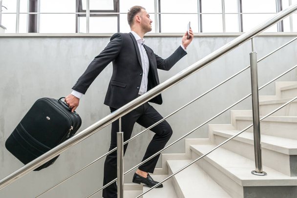 Biznesmen trzymający walizkę biegającą po schodach w nowoczesnym budynku - Zdjęcie, obraz