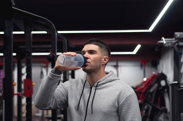 Muscular men drinks protein or water, energy drink in the gym. Sportsman holding a shaker with copy space - Foto, imagen