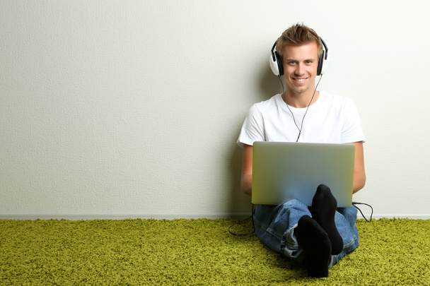 Young man relaxing on carpet and listening to music, on gray wall background - Φωτογραφία, εικόνα