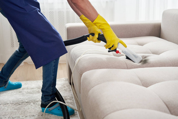 Close-up of housekeeper holding modern washing vacuum cleaner and cleaning dirty sofa with professionally detergent. Professional springclean at home concept - Fotó, kép