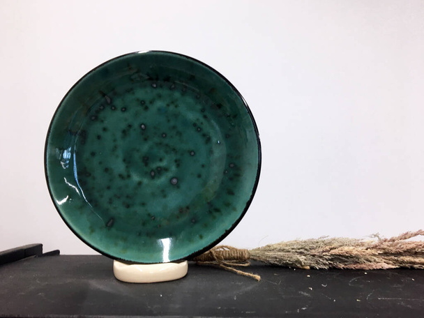 Duży zielony piękny dekoracyjny ceramiczny talerz na drewnianej półce w sklepie dekoracyjnym. Ręcznie robiona miska. Ceramiczna miska z postrzępionymi krawędziami. Jagged Mouth Bowl. Szafka z naczyniami - Zdjęcie, obraz