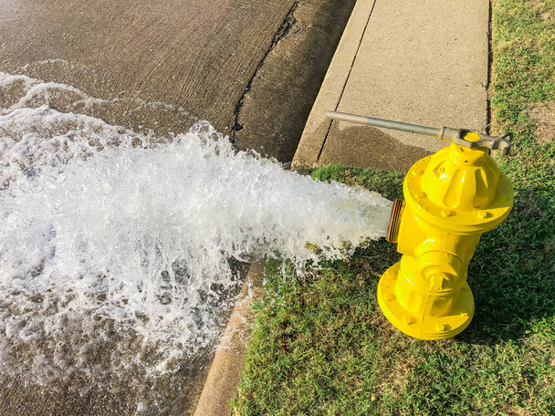 Вгорі видніється жовтий вогняний гідрант, що розливає воду через житлову вулицю біля Далласа (штат Техас, США). - Фото, зображення