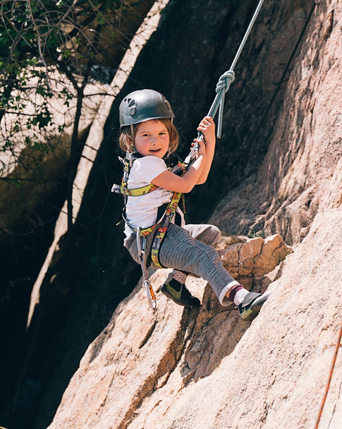 Young girl smiling and having fun while she does rock climbing. She is looking at camera. - Photo, Image