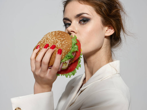 Beautiful young woman with make-up holds a hamburger - Zdjęcie, obraz