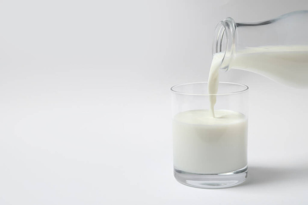 Pouring milk into glass on white background - Foto, afbeelding