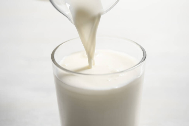 Pouring milk into glass on white table, closeup - Foto, imagen