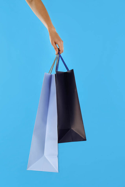 Woman with paper shopping bags on light blue background, closeup - Fotografie, Obrázek
