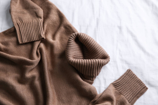 Brown warm sweater on white crumpled fabric, top view - 写真・画像
