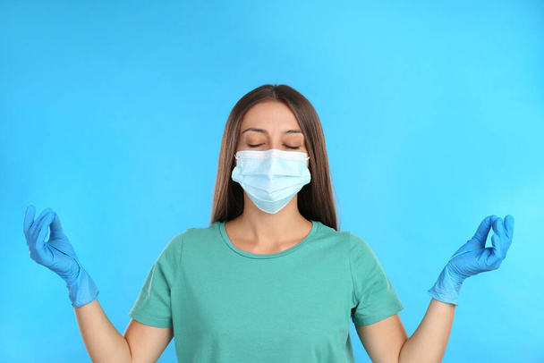 Woman in protective mask meditating on light blue background. Dealing with stress caused by COVID?19 pandemic - Foto, Imagem
