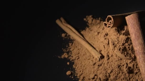 Κανέλα και κανέλα σε σκόνη περιστρεφόμενη σε μαύρο φόντο - Πλάνα, βίντεο