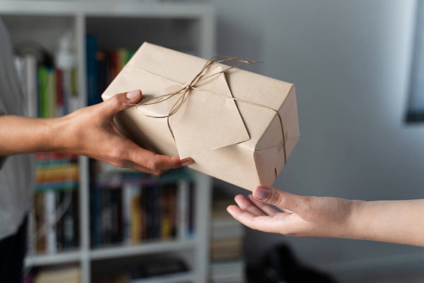 Close up on hands of unknown caucasian woman holding wrapped gift box birthday present handing to the other female person at home or office in day - giving and receiving concept - Foto, imagen