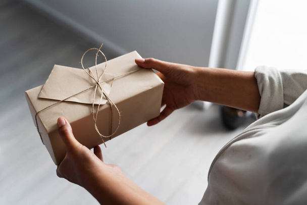Вид сверху на руки неизвестной кавказки, держащей завернутую подарочную коробку на день рождения дома или в офисе - дарение и получение концепции - Фото, изображение