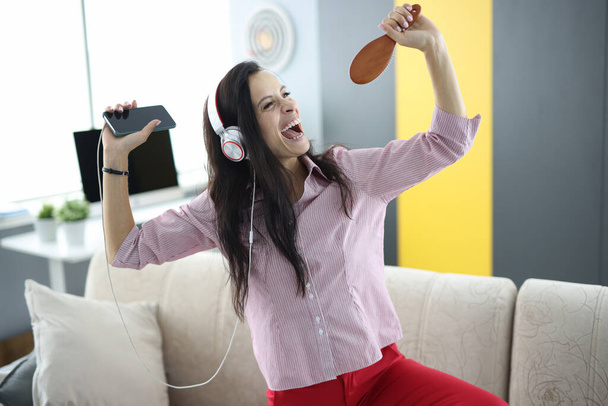 Жінка в навушниках на дивані тримає смартфон в руках і робить вигляд, що співає
 - Фото, зображення