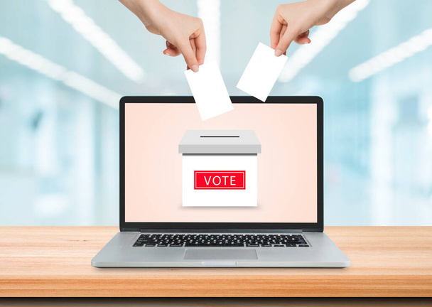 Концепция онлайн-голосования: Держать и класть бумажную карту для голосования в урну для голосования на экране ноутбука. - Фото, изображение