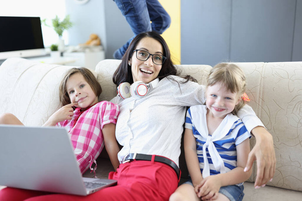 Mosolygó nő ül laptop és a gyerekek a kanapén. - Fotó, kép
