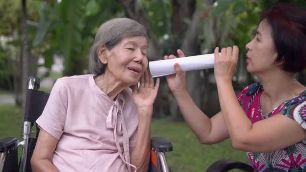 Κόρη μιλάει σε ηλικιωμένη γυναίκα με προβλήματα ακοής, χρησιμοποιώντας χάρτινο σωλήνα - Πλάνα, βίντεο