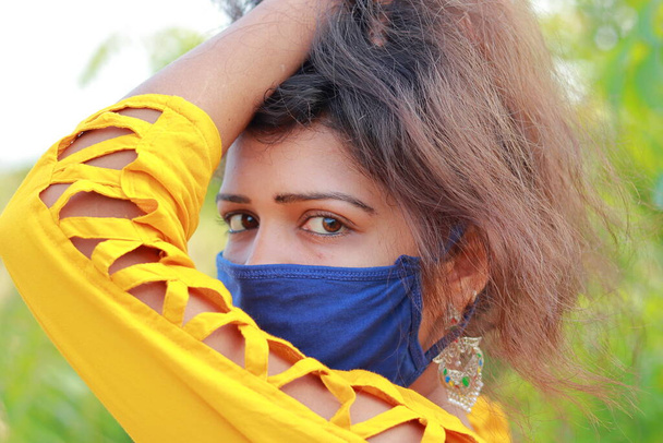 Una atractiva joven india posa en la naturaleza con una máscara facial para evitar una enfermedad potencialmente mortal como Corona. - Foto, Imagen