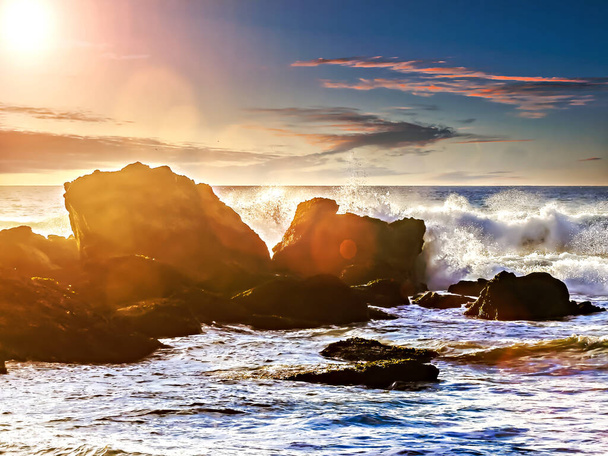 Seelandschaft mit Wellen, die bei Sonnenuntergang an den Felsen brechen, mit einem Himmel in Orangetönen - Foto, Bild
