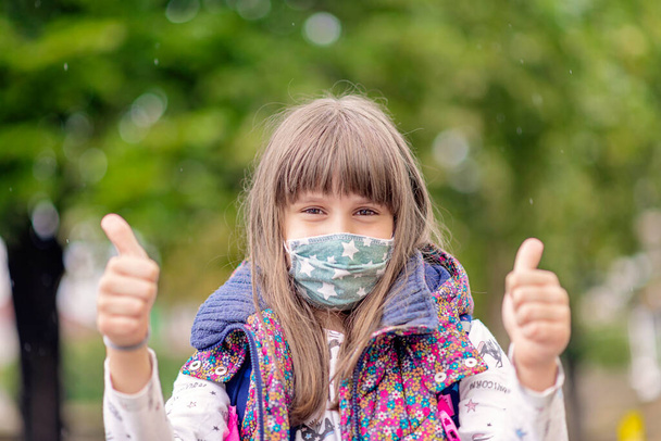 Girl wearing face mask during corona virus and flu outbreak. Back to school concept, thumbs up for seeing friends again. Cutegirl looking at the camera.  - Photo, Image