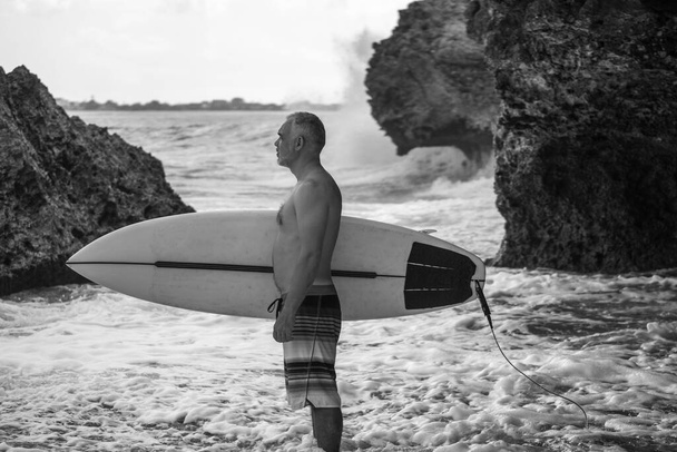 Portrait of handsome shirtless man surfer, holding white surf board and green cactus on background in Bali - Fotografie, Obrázek