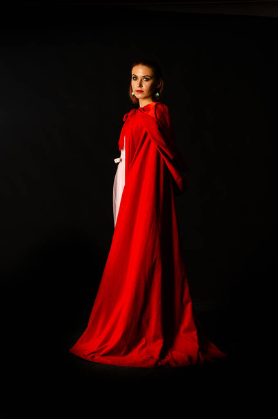 Piękna kobieta w czerwonym płaszczu w studio. Czerwony Kapturek. Dramatyczne i fantastyczne fotografowanie, modne tonowanie. Jak księżniczka.. - Zdjęcie, obraz