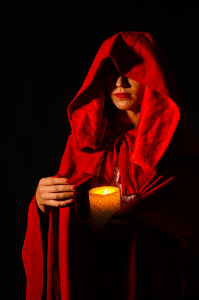 krásná žena v červeném plášti se svíčkou ve studiu. Žena Červená Karkulka. Dramatické a fantastické natáčení, módní tónování.  - Fotografie, Obrázek