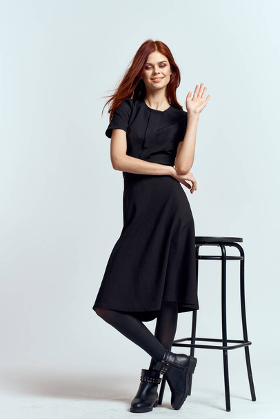 woman high chair indoors full length black dress red hair model boots - Foto, afbeelding