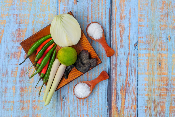 Деревянная тарелка с солью, msg, имбирь, чеснок, лук, ключ лайм, чили и лимонной травой над деревянной доской. - Фото, изображение