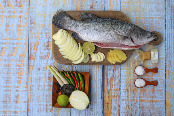 Barramundi or asian seabass fish with salt, msg,ginger,garlic,onion,key lime, chilies and lemongrass over the wooden cutting board. - Photo, Image