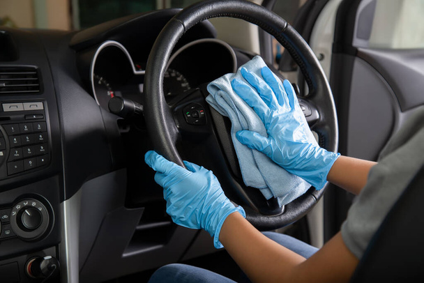 Ellerinde lastik eldiven, direksiyon simidini mikrofiber bezle temizliyor, arabanın içini temizliyor.. - Fotoğraf, Görsel
