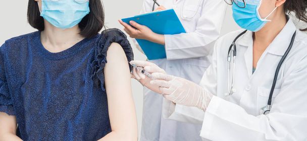 Szczepienie pasztetu. Kobieta-lekarz pozywający strzykawkę podającą szczepionkę kobiecie w szpitalu, nosząca maskę medyczną w celu ochrony przed rozprzestrzenianiem się wirusa, koncepcja opieki zdrowotnej typu kopiuj-przestrzeń  - Zdjęcie, obraz