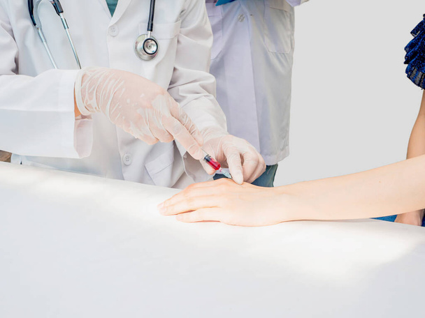  close-up handen van de arts injectiespuit gebruiken om patiënten handen doen bloedonderzoek met stagiair naast en het nemen van nota. witte kopieerruimte, medisch zorgconcept - Foto, afbeelding