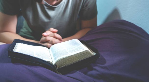 nő imádkozik az ágyon reggel, könyv vagy szent biblia megnyitása előtt személy meghajtó fej és kéz imádkozás, keresztény koncepció, imádkozik a világválság,  - Fotó, kép
