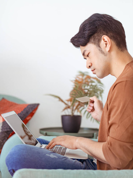 Jeune homme faisant du shopping en ligne avec carte de crédit et ordinateur portable à la maison - Photo, image