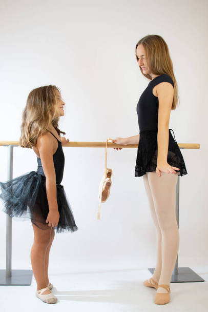 Δάσκαλος της σχολής μπαλέτου βοηθά τη νεαρή μπαλαρίνα να εκτελέσει διαφορετικές χορογραφικές ασκήσεις. Κάνουν πρόβες στο μπαλέτο. Ο δάσκαλος επικοινωνεί με το κοριτσάκι.. - Φωτογραφία, εικόνα