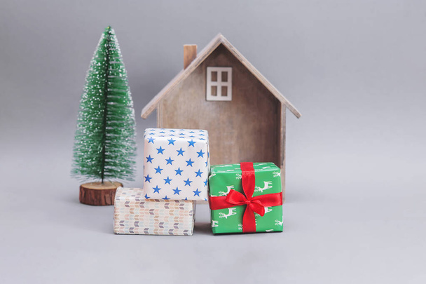 Wooden small house with gifts and Christmas tree against gray background. New Year's composition. Christmas presents. - Photo, image