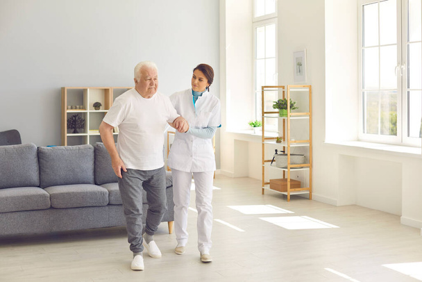 Healthcare worker helping senior man to walk in office of modern hospital or geriatric rehab center - Photo, Image