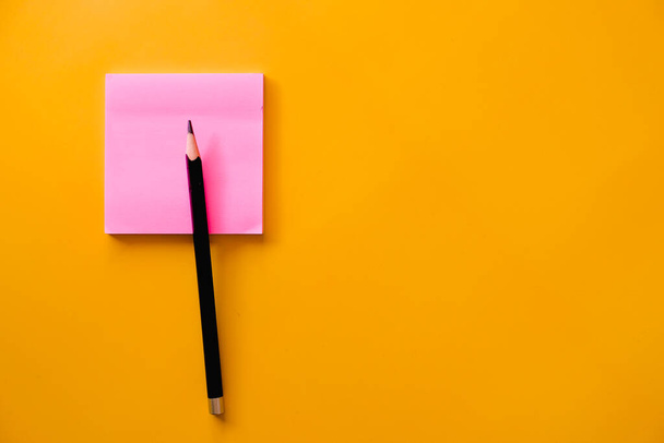 Schwarzer Bleistift und rosa Notizpapier auf gelbem Hintergrund - Foto, Bild
