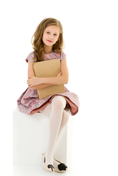 Schönes Mädchen sitzt auf White Cube und umarmt Buch - Foto, Bild