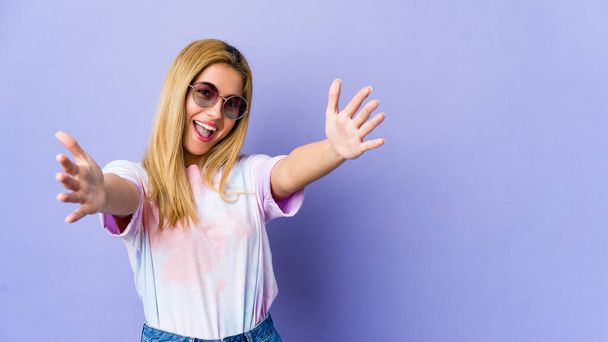 Mladý hipík žena s brýlemi izolované na fialovém pozadí cítí jistý dávat objetí na kameru. - Fotografie, Obrázek