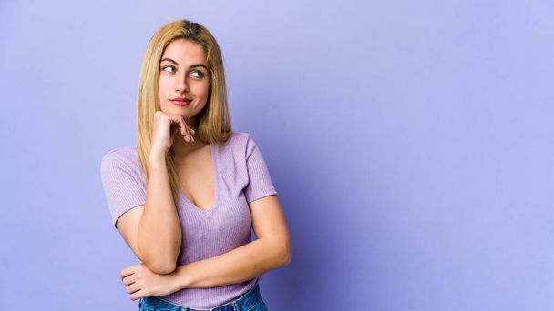 Young blonde woman isolated on purple background relaxed thinking about something looking at a copy space. - Foto, afbeelding