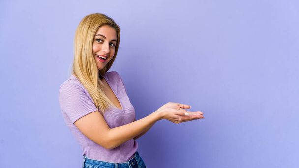 Young blonde woman isolated on purple background holding a copy space on a palm. - Fotó, kép