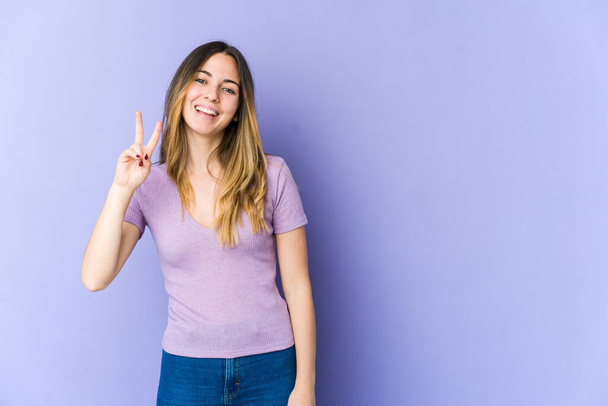 Молода біла жінка ізольована на фіолетовому фоні, показуючи знак перемоги і посміхаючись широко
. - Фото, зображення