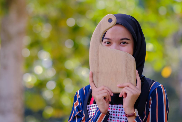 Gyönyörű nő visel hidzsáb gazdaság fa vágódeszka és fa merőkanál egy kötény homályos háttér. - Fotó, kép